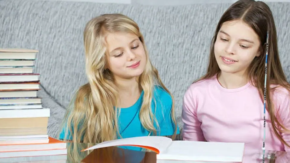 two smiling girls reading a book
