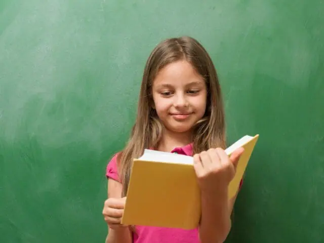 1st grader reading book with school blackboard background